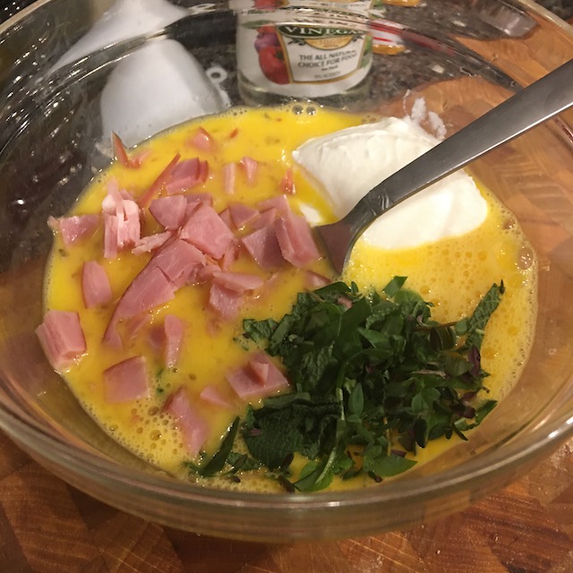 A bowl showing a mixture of egg, chopped ham, fresh herbs, and yogurt.